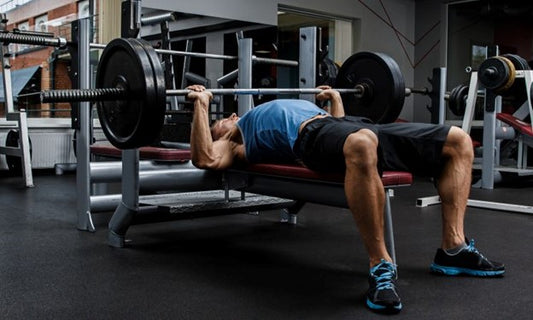 man performing the barbell bench press on an Olympic weight bench at a gym